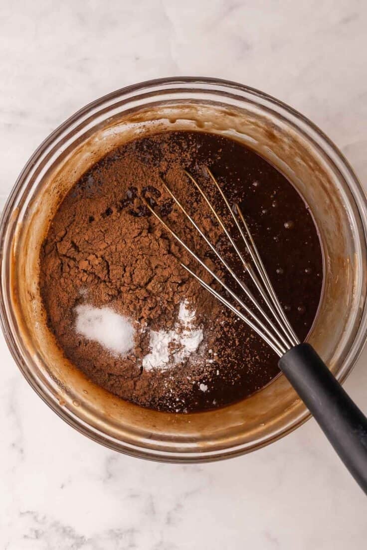 cocoa added to chocolate in glass bowl with whisk in it.