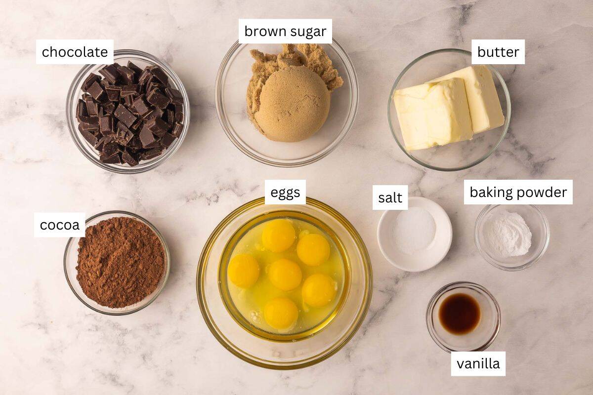 This Flourless Chocolate Cake is rich, fudgy, and naturally gluten-free. Easy to make with simple ingredients like melted chocolate, eggs and butter, it’s the perfect chocolate lover’s dessert! #chocolate #dessert #recipe | chocolate dessert | dessert recipes | the recipe rebel | easy recipes | valentine's day dessert | valentine's day recipe ingredients needed for flourless chocolate cake in bowls.