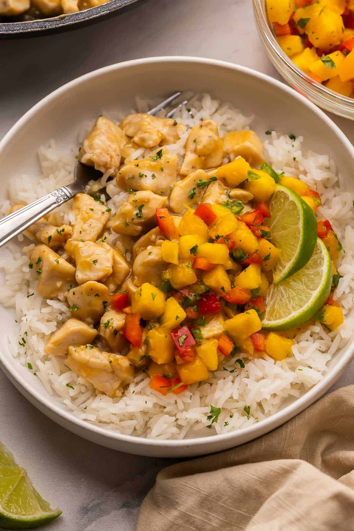 These Mango Chicken Rice Bowls with tender chicken breast, fluffy rice and homemade mango salsa are ready in just 35 minutes and perfect for weeknight dinners! #chicken #recipe #dinner | dinner ideas | dinner recipes | chicken breast recipes | chicken recipes | easy dinner ideas | healthy meals close up image of mango chicken rice bowls with mango salsa and lime wedges.