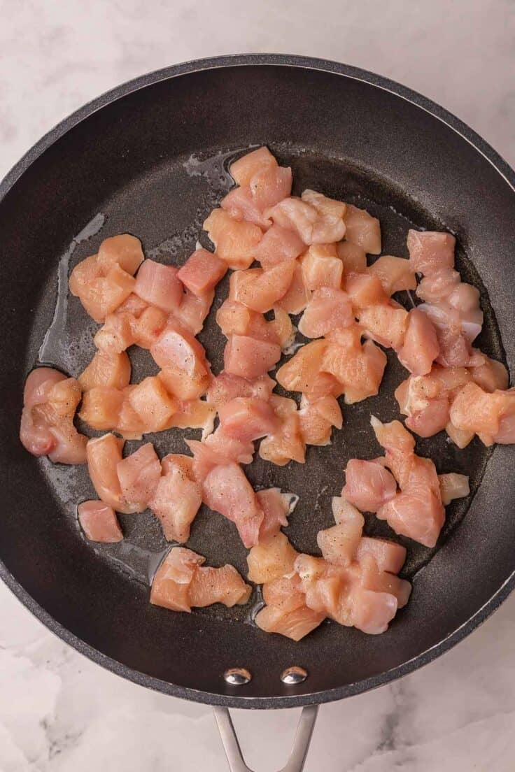 chicken pieces searing in black skillet.