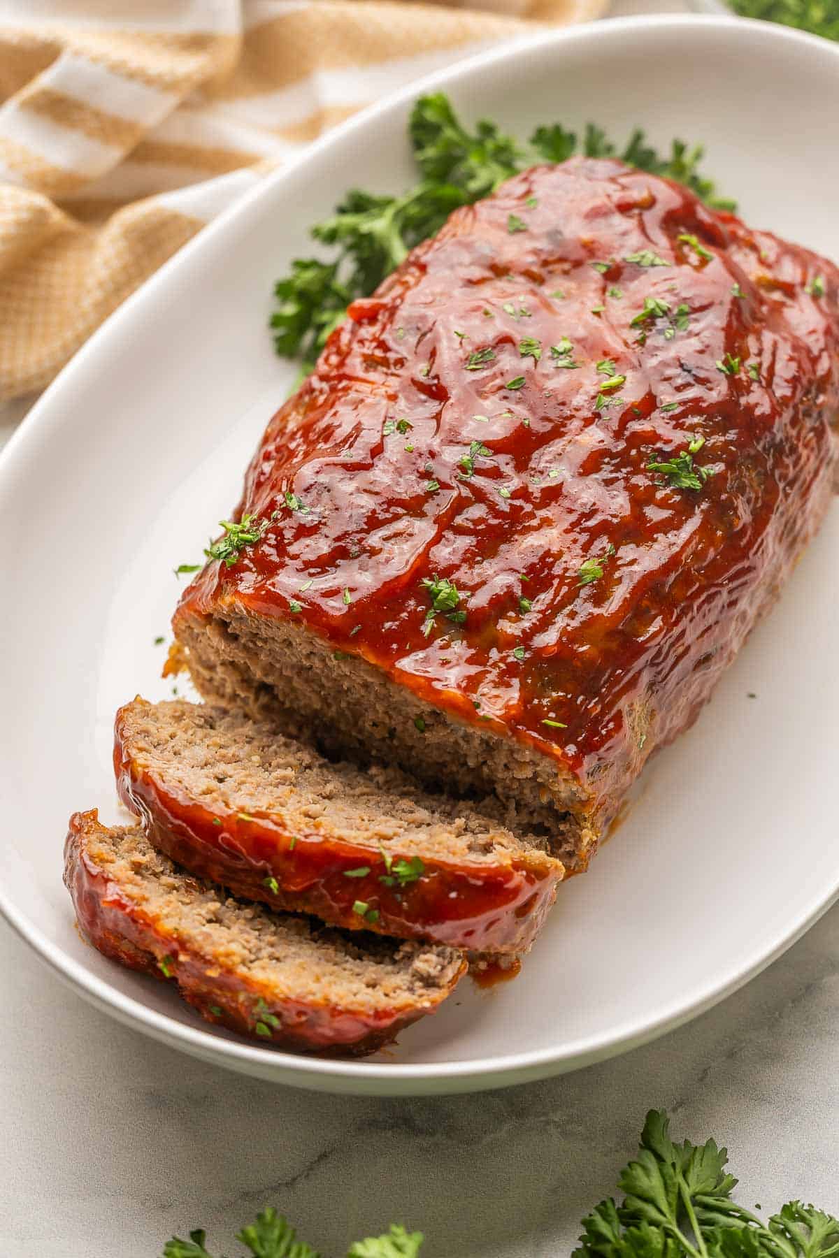 This truly is the BEST Meatloaf Recipe! It's juicy, flavorful, and topped with a sweet ketchup glaze. It's easy, comforting, and also makes a great freezer meal. #groundbeef #dinner #recipe | dinner ideas | dinner recipes | ground beef recipes | ground pork | comfort food | the recipe rebel | make ahead meals | freezer meals large white platter with sliced meatloaf on it.
