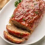 meatloaf that has been sliced on a platter topped with chopped parsley.