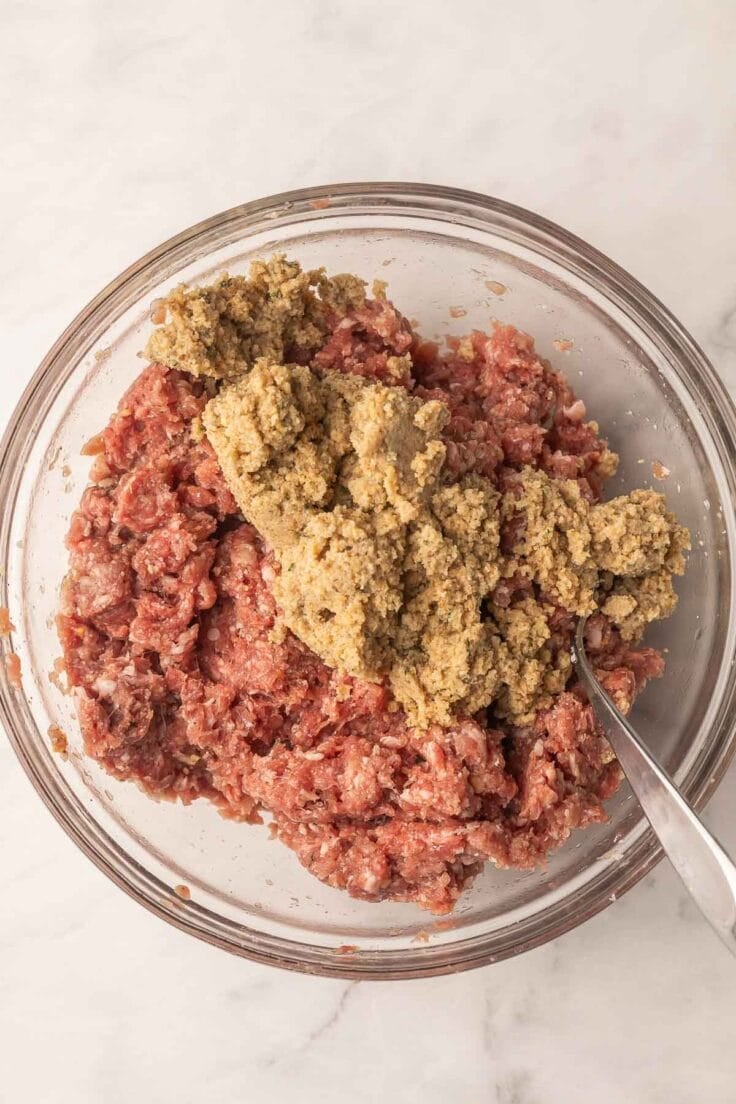 breadcrumbs added to meatloaf ingredients in glass mixing bowl.
