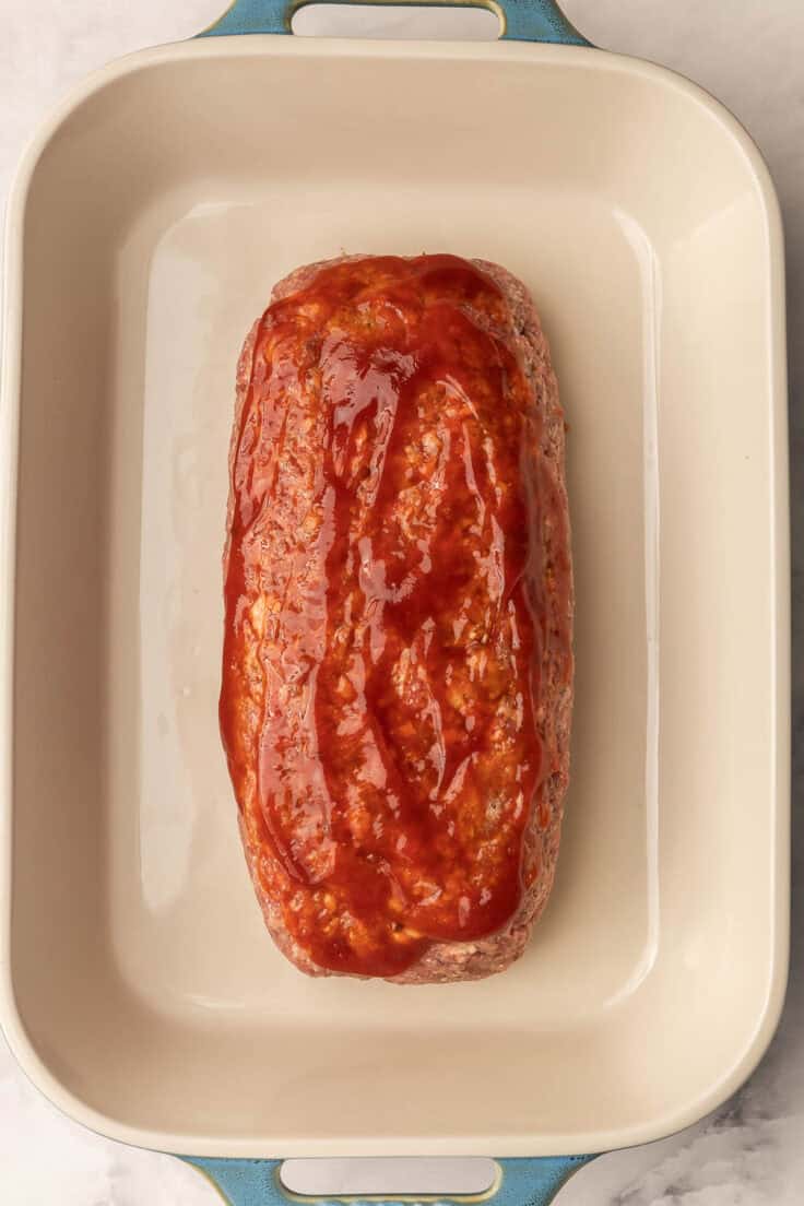 uncooked meatloaf in baking dish with sauce spread on top.
