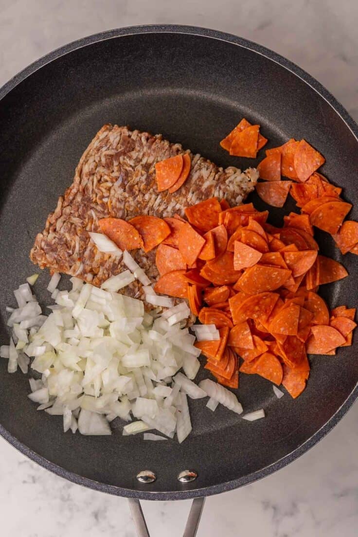 meat and chopped onions in black frying pan.