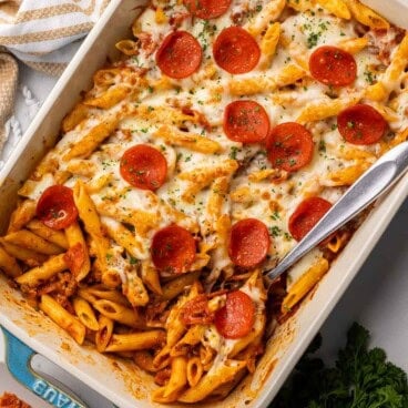 a steel ladle in the pan of pizza pasta with parsley beside.
