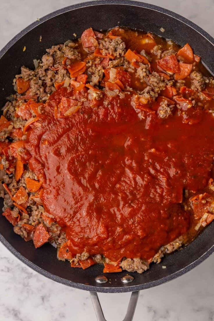 marinara sauce added to meat sauce ingredients in pan.