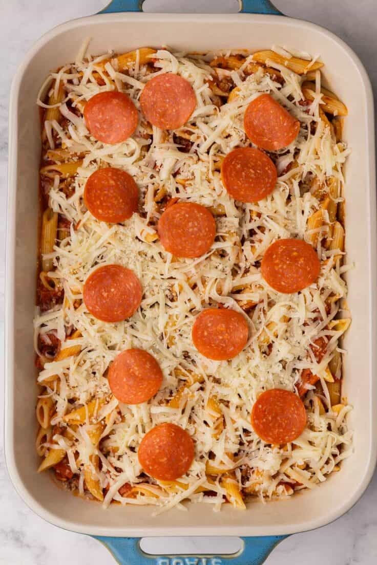 shredded cheese and pepperoni added to pizza pasta in baking dish.