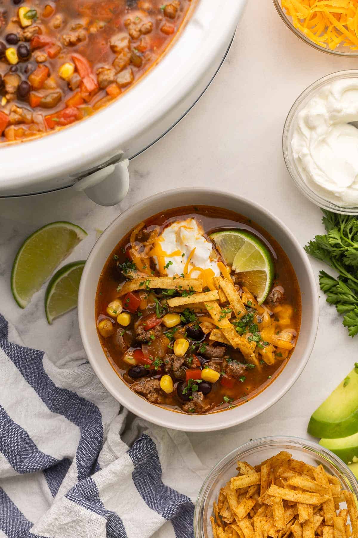 This Slow Cooker Taco Soup is an easy crockpot meal that's packed with flavor! Just 15 minutes of prep and the crockpot does the rest. Perfect for busy nights when you don't feel like cooking! overhead image of bowl of taco soup with slow cooker on the side.