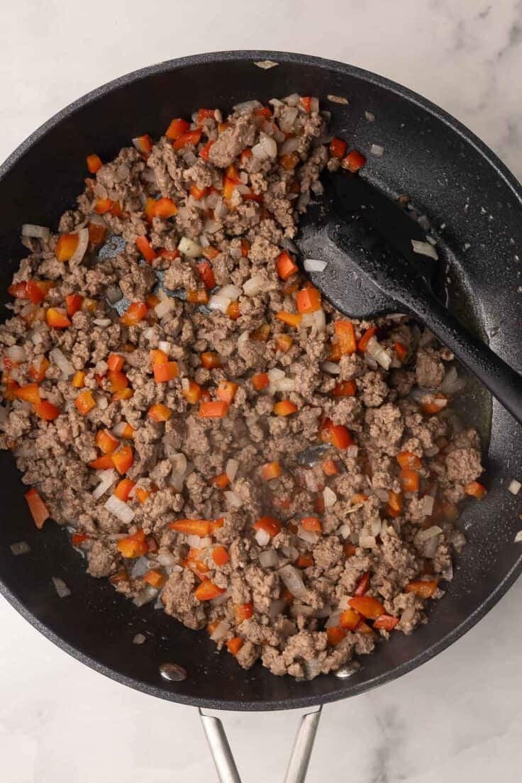 cooked ground beef with peppers and onions in black skillet.