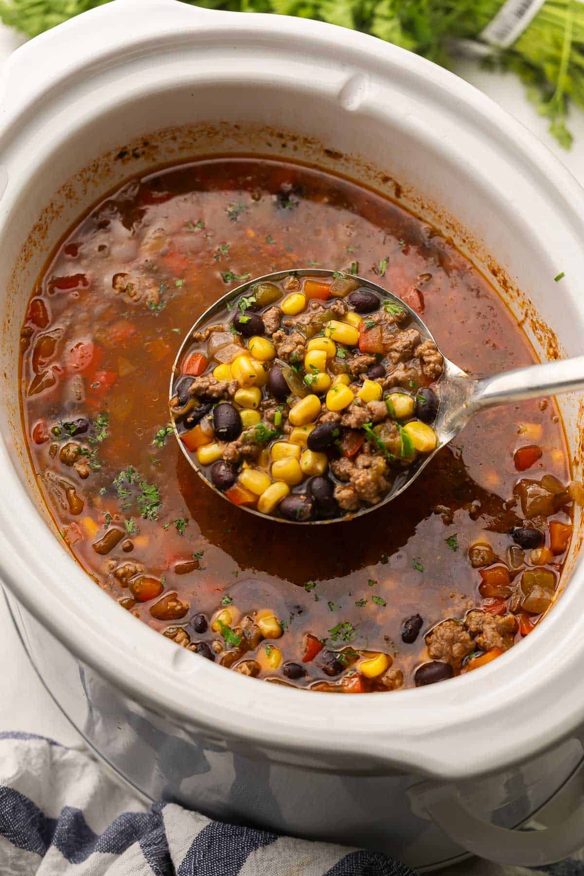 slow cooker taco soup in a white crockpot with a metal ladle.