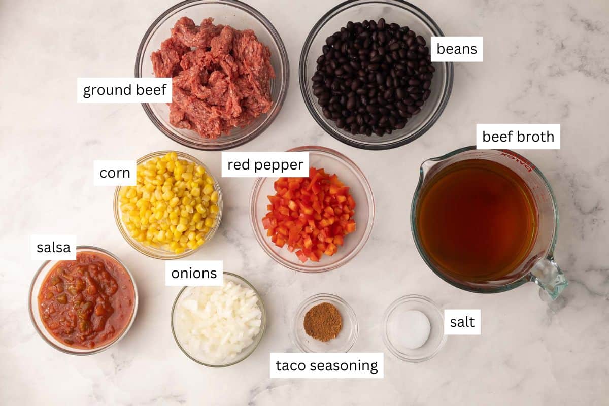 This Slow Cooker Taco Soup is an easy crockpot meal that's packed with flavor! Just 15 minutes of prep and the crockpot does the rest. Perfect for busy nights when you don't feel like cooking! #soup #dinner #recipe | soup recipes | slow cooker soup | crockpot soup | ground beef recipes overhead image of crockpot taco soup ingredients on white background.