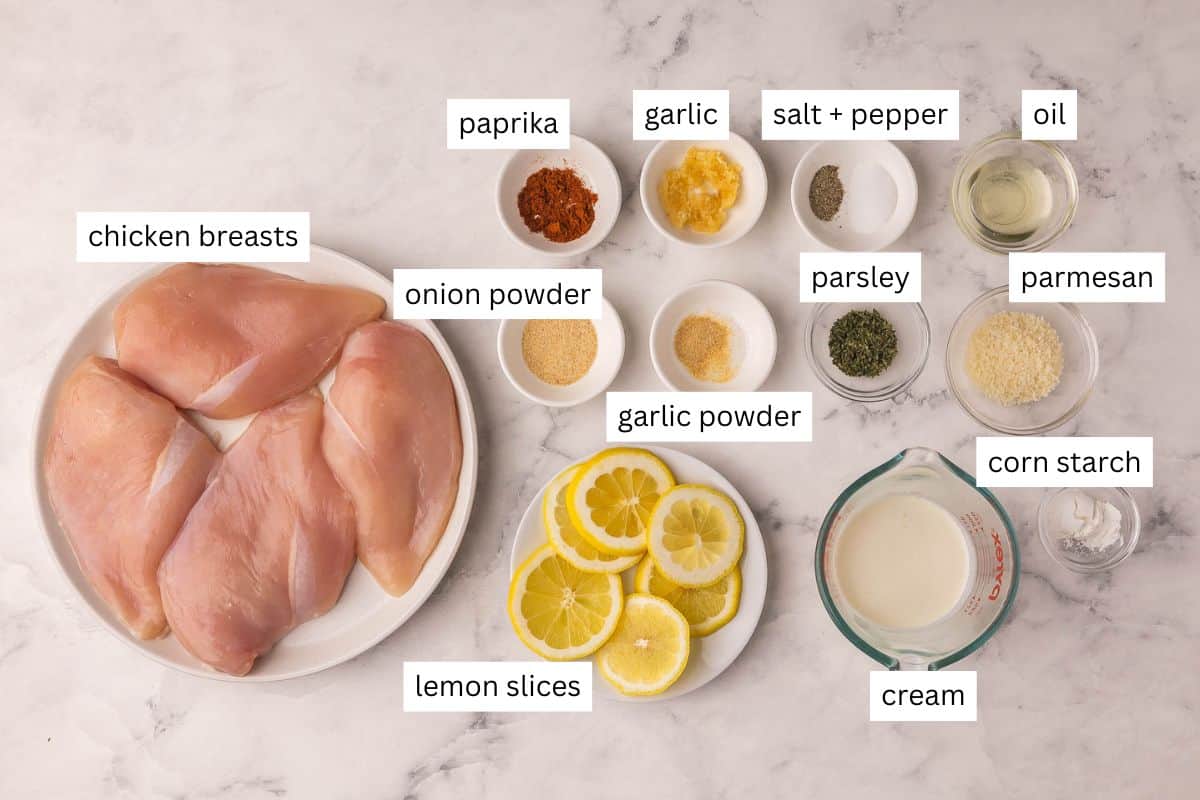 This creamy baked Lemon Chicken comes together in 30 minutes with simple ingredients and tons of flavor! Made with juicy, tender chicken breast baked in a garlicky lemon-Parmesan sauce. #chicken #recipe #dinner | dinner ideas | dinner recipes | chicken breast recipes | lemon recipes | comfort food | quick meals overhead image of lemon chicken breast ingredients on a marble background.