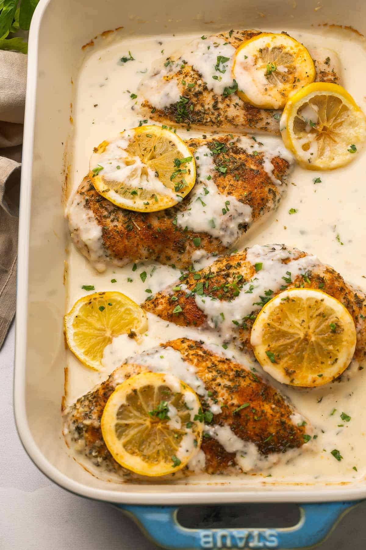 This creamy baked Lemon Chicken comes together in 30 minutes with simple ingredients and tons of flavor! Made with juicy, tender chicken breast baked in a garlicky lemon-Parmesan sauce. #chicken #recipe #dinner | dinner ideas | dinner recipes | chicken breast recipes | lemon recipes | comfort food | quick meals chicken breasts in a baking dish with creamy lemon sauce.
