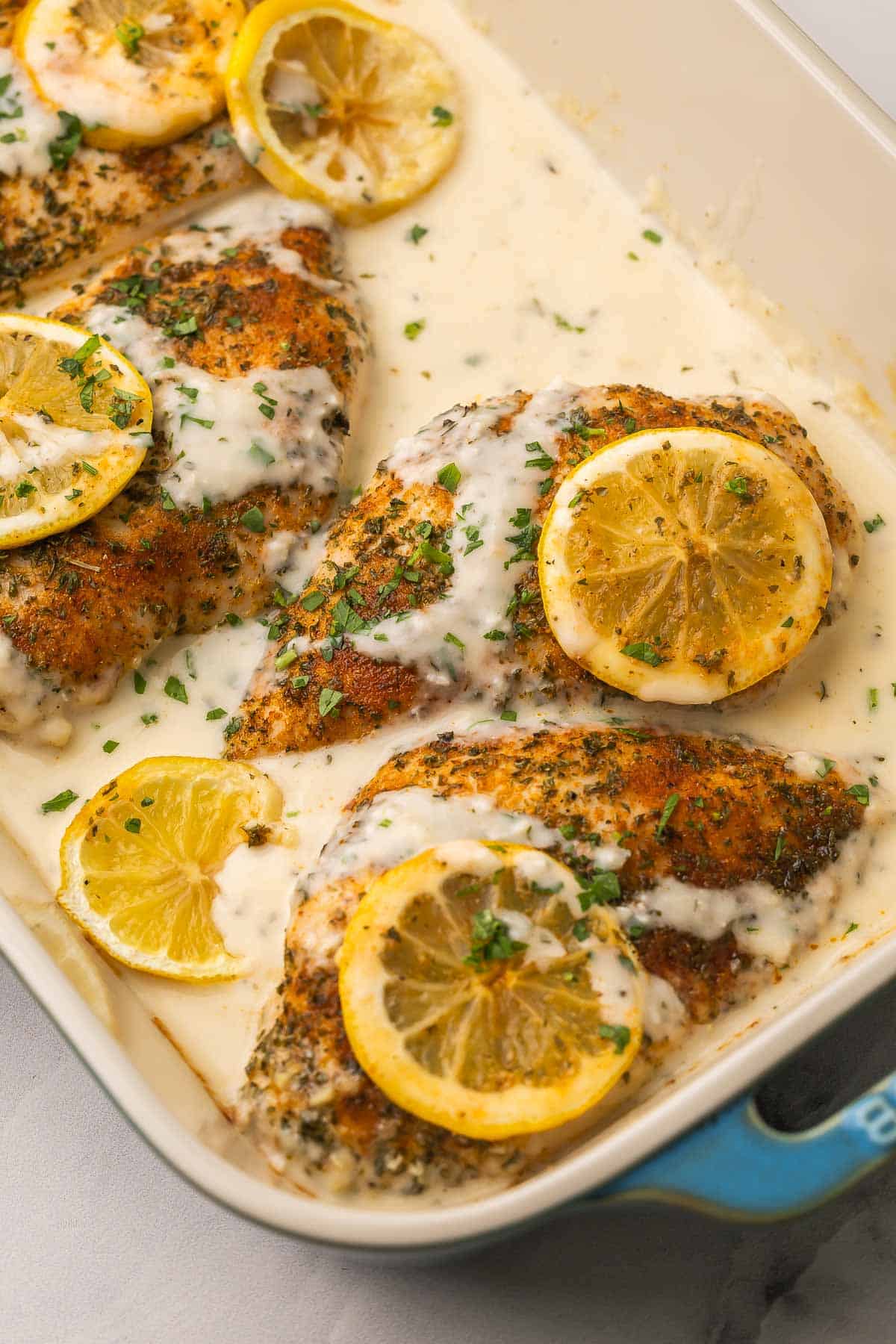 This creamy baked Lemon Chicken comes together in 30 minutes with simple ingredients and tons of flavor! Made with juicy, tender chicken breast baked in a garlicky lemon-Parmesan sauce. #chicken #recipe #dinner | dinner ideas | dinner recipes | chicken breast recipes | lemon recipes | comfort food | quick meals close up image of creamy lemon chicken breast in baking dish.