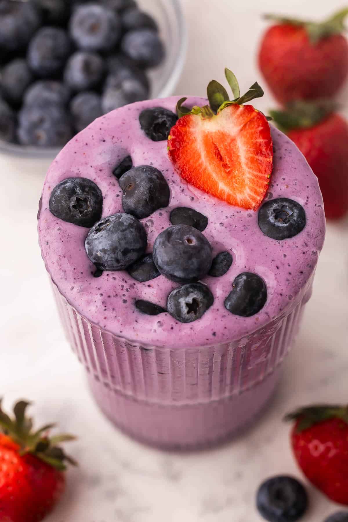 This easy Mixed Berry Smoothie is creamy, refreshing, and packed with strawberries, blueberries and raspberries! Ready in 5 minutes and is the perfect healthy breakfast or snack. #breakfast #smoothie #drink | summer drinks | healthy snack | healthy breakfast | blueberry | strawberry | raspberry close up overhead image of mixed berry smoothie with fresh blueberries and strawberry slice on top.