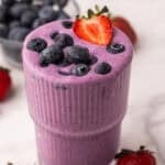 square image of berry smoothie in a glass with blueberries and strawberries on top.