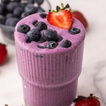 square image of berry smoothie in a glass with blueberries and strawberries on top.