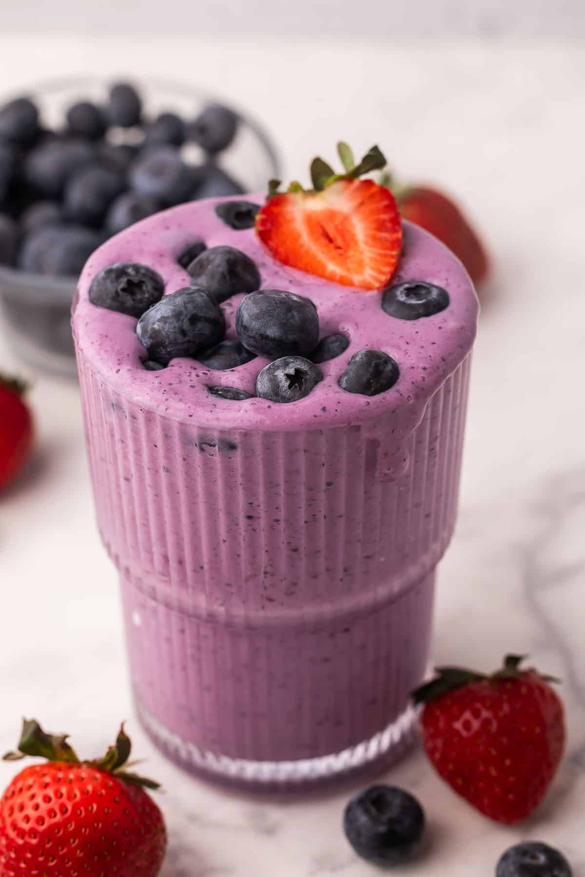 This easy Mixed Berry Smoothie is creamy, refreshing, and packed with strawberries, blueberries and raspberries! Ready in 5 minutes and is the perfect healthy breakfast or snack. #breakfast #smoothie #drink | summer drinks | healthy snack | healthy breakfast | blueberry | strawberry | raspberry mixed berry smoothie recipe in a glass with blueberries and strawberry on top.