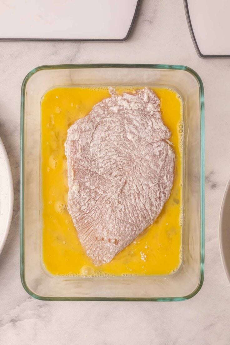 chicken breasts dusted with flour in bowl with eggs.