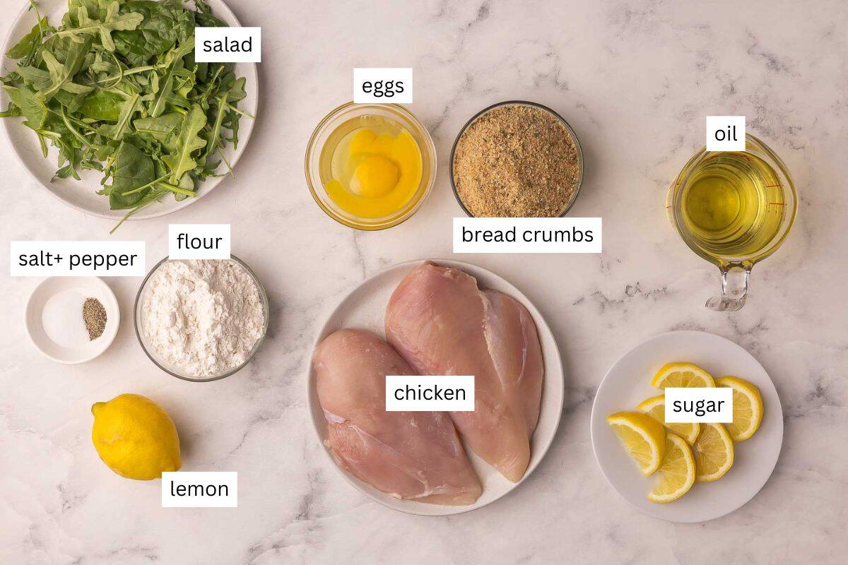 Crispy Chicken Milanese is golden, crunchy, and ready in 30 minutes! Thin chicken cutlets coated in breadcrumbs and pan-fried until perfectly crisp. Perfect with a squeeze of lemon and some fresh greens! #chicken #dinner #recipe | italian food | italian recipes | crispy chicken | breaded chicken | chicken recipes | chicken breast ingredients for chicken milanese on a white marble background.
