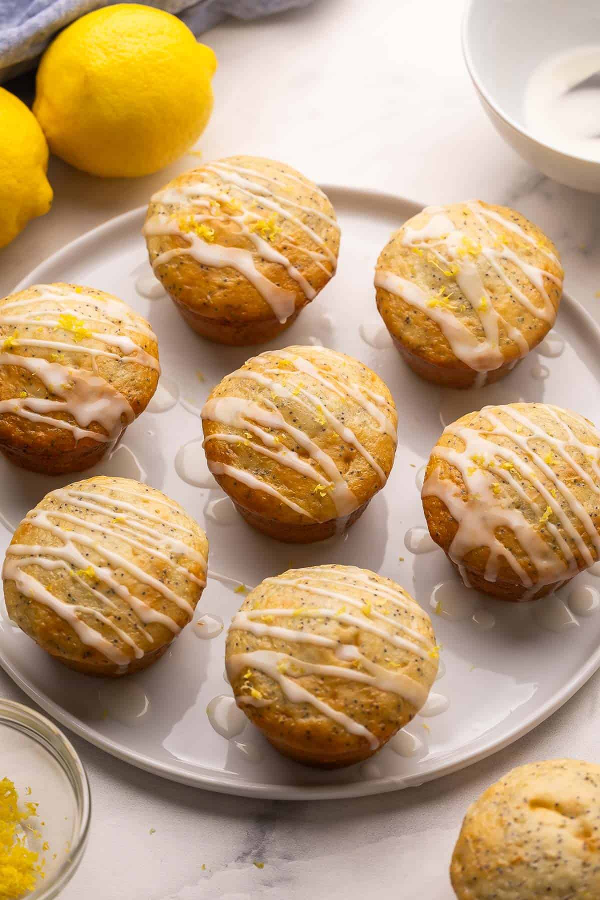 These fluffy Lemon Poppy Seed Muffins are light, zesty, and bakery-soft! Made with Greek yogurt for moisture and finished with a bright lemon glaze. #baking #recipe | muffin recipes | lemon recipes | baking from scratch | breakfast ideas | healthy snacks plate of lemon poppy seed muffins with glaze.
