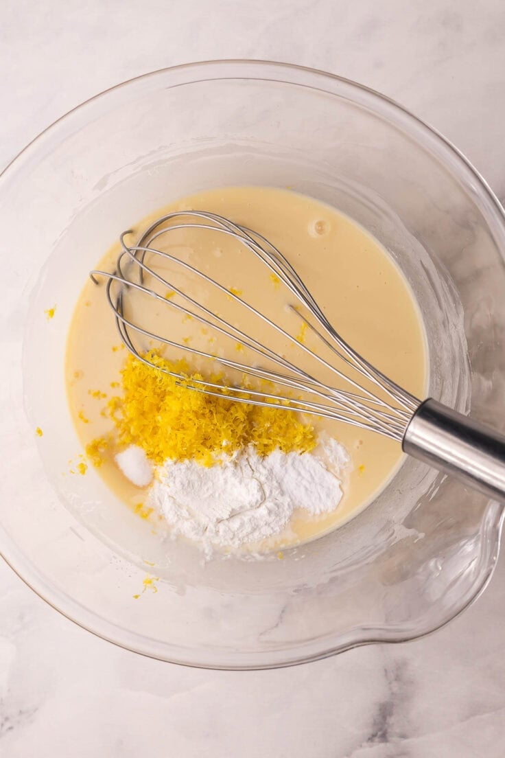 lemon zest and leavening agents added to wet ingredients in mixing bowl.