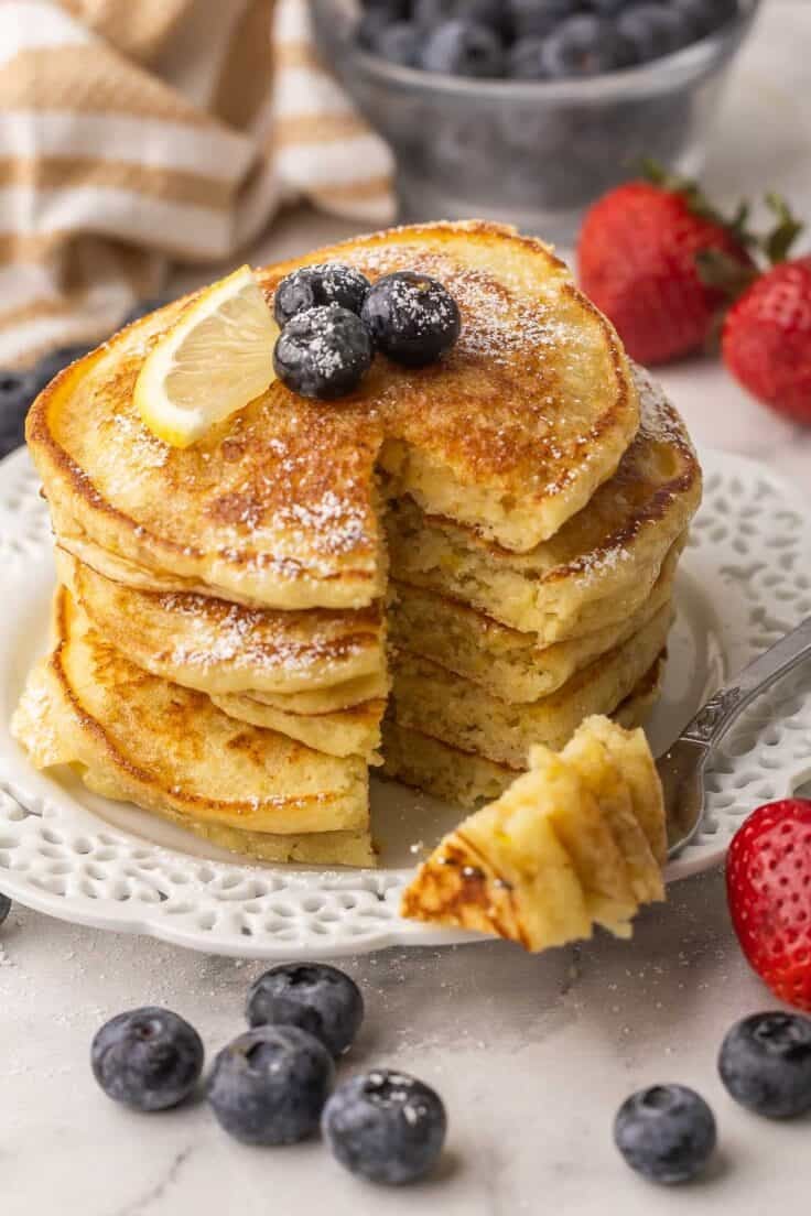 one bite cut out of stack of lemon pancakes on a plate.