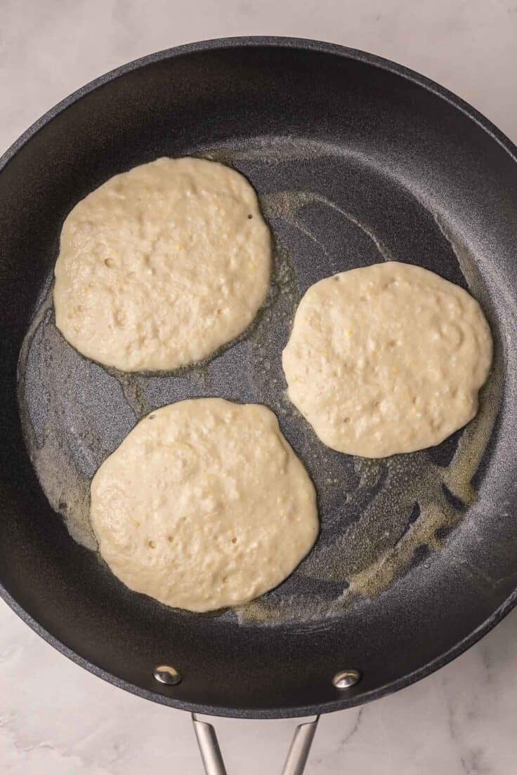 lemon ricotta pancakes cooking in black skillet.