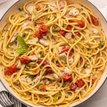 square overhead image of creamy tomato basil pasta with chicken in white braiser.