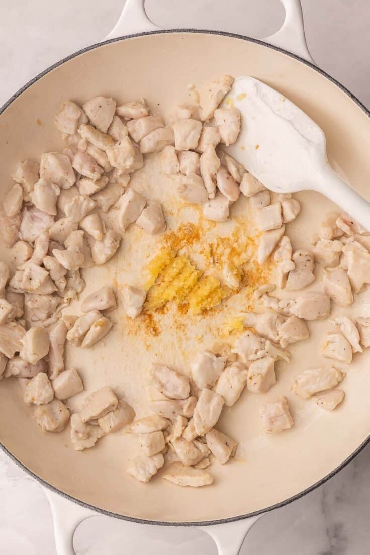 chicken cooking in a white skillet with garlic.