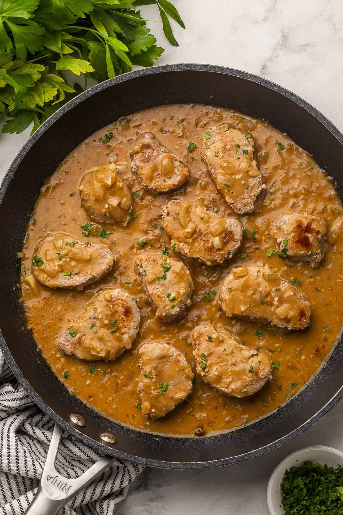 These Pork Medallions with Balsamic Onion Gravy are full of flavor, with a perfectly seasoned creamy gravy with sautéed onions and a touch of vinegar. Ready in 30 minutes with simple ingredients and one skillet! #pork #dinner #recipe | easy dinner ideas | pork tenderloin recipes | easy dinner | comfort food | pork with gravy | overhead image of pork medallions with onion gravy and fresh parsley.