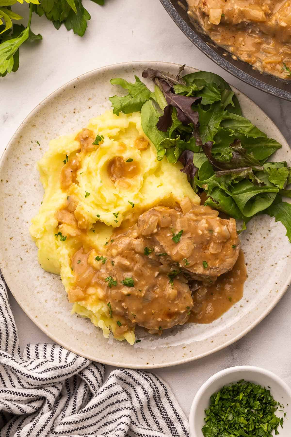 These Pork Medallions with Balsamic Onion Gravy are full of flavor, with a perfectly seasoned creamy gravy with sautéed onions and a touch of vinegar. Ready in 30 minutes with simple ingredients and one skillet! #pork #dinner #recipe | easy dinner ideas | pork tenderloin recipes | easy dinner | comfort food | pork with gravy | pork medallions on a plate with mashed potatoes and greens.