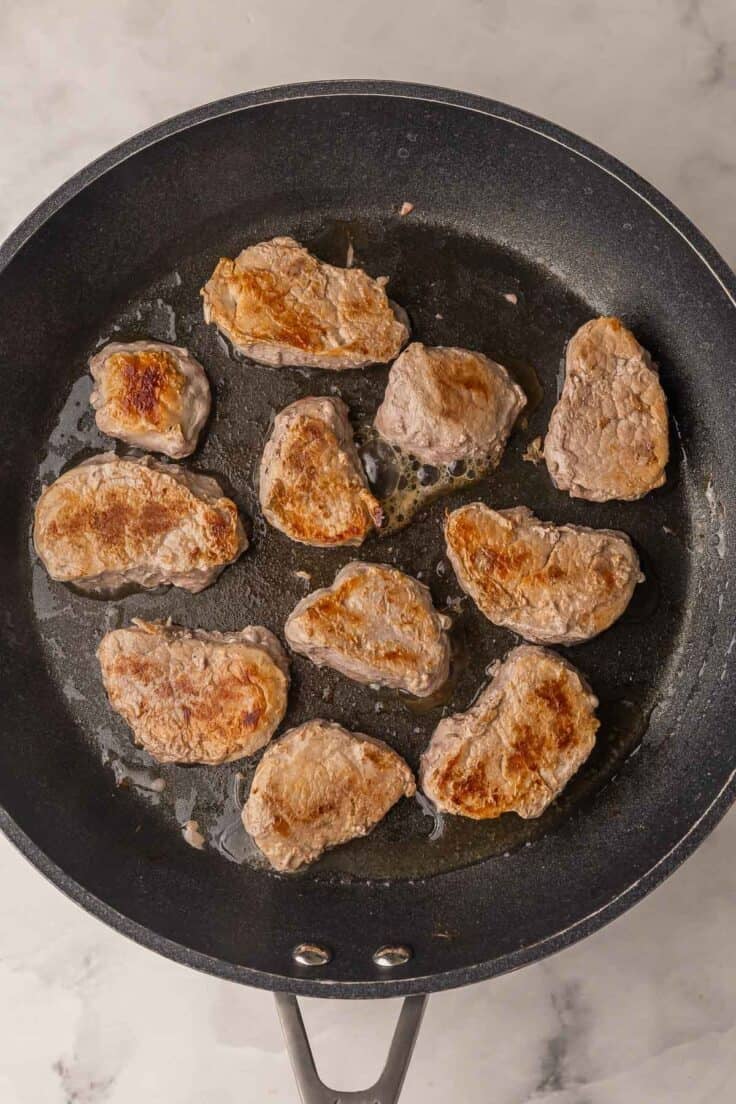 searing pork medallions in black skillet.