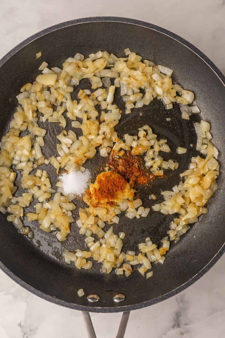 onions cooking in black skillet with spices.