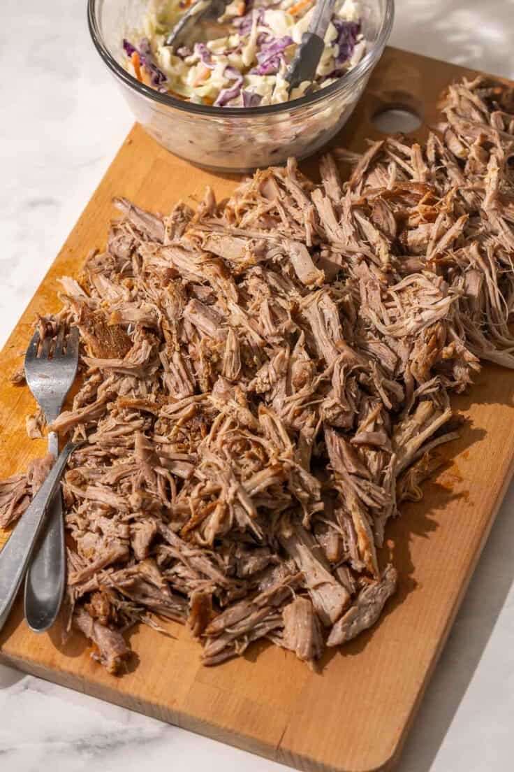 close up image of pulled pork with two forks and coleslaw on a wooden cutting boar.