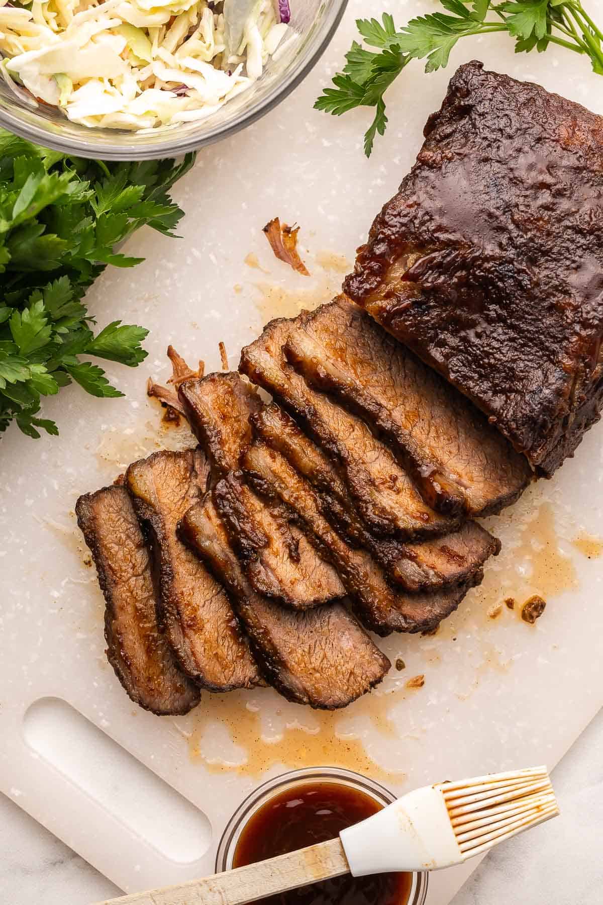 This Slow Cooker Beef Brisket is tender, juicy, and packed with sweet and smoky flavor from a homemade spice rub. It’s the easiest way to make fall-apart brisket right at home without a smoker or grill! #beef #recipe #dinner | barbecue beef | bbq | beef recipes | slow cooker recipes | crockpot meals sliced beef brisket with coleslaw and BBQ sauce beside.