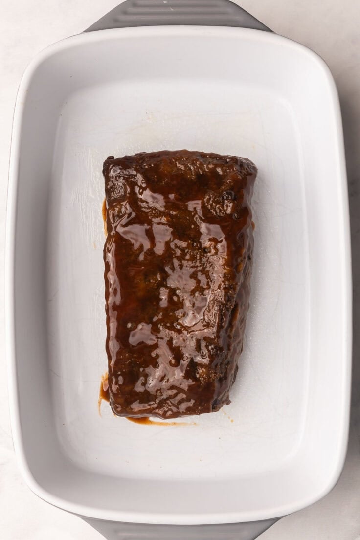beef brisket in a baking dish topped with BBQ sauce.