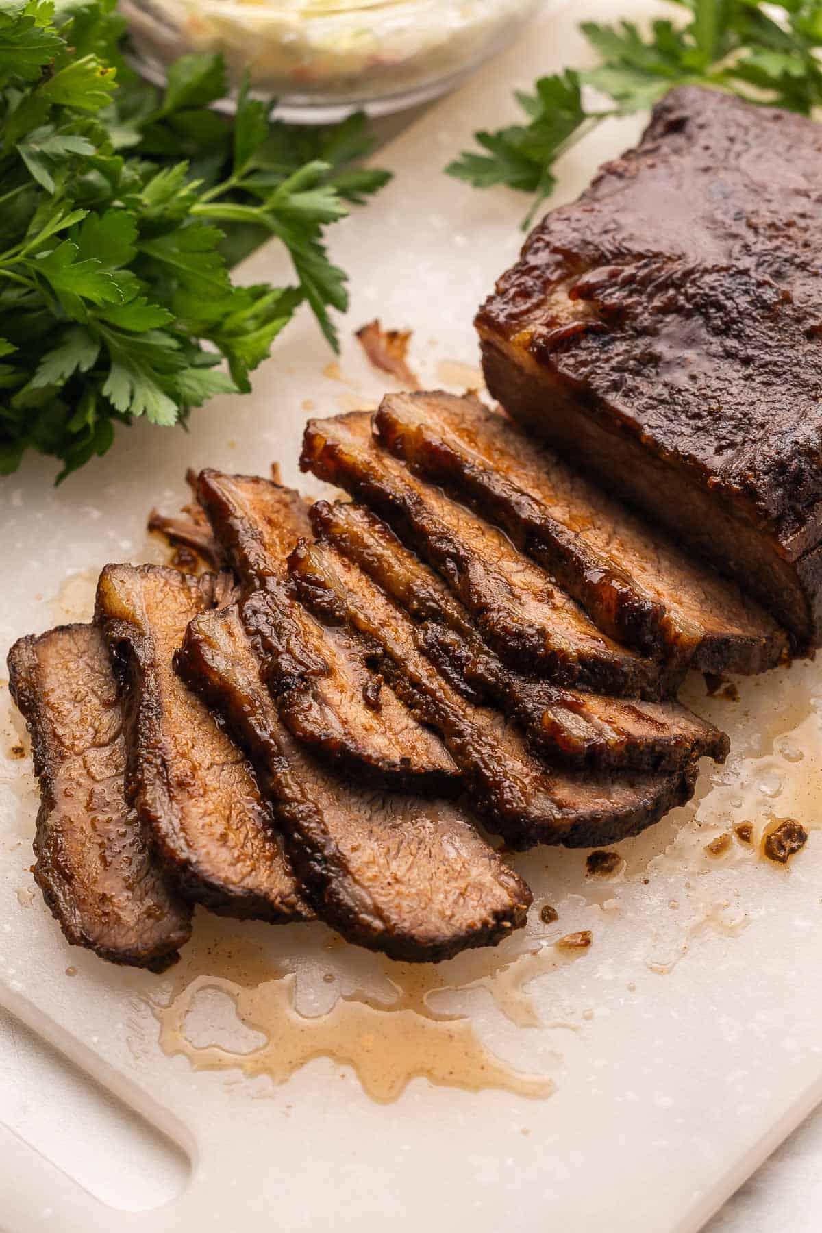 This Slow Cooker Beef Brisket is tender, juicy, and packed with sweet and smoky flavor from a homemade spice rub. It’s the easiest way to make fall-apart brisket right at home without a smoker or grill! #beef #recipe #dinner | barbecue beef | bbq | beef recipes | slow cooker recipes | crockpot meals white cutting board with sliced beef brisket on it.