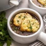 square image of slow cooker french onion soup in a white bowl with cheese toast on top.