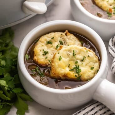 square image of slow cooker french onion soup in a white bowl with cheese toast on top.