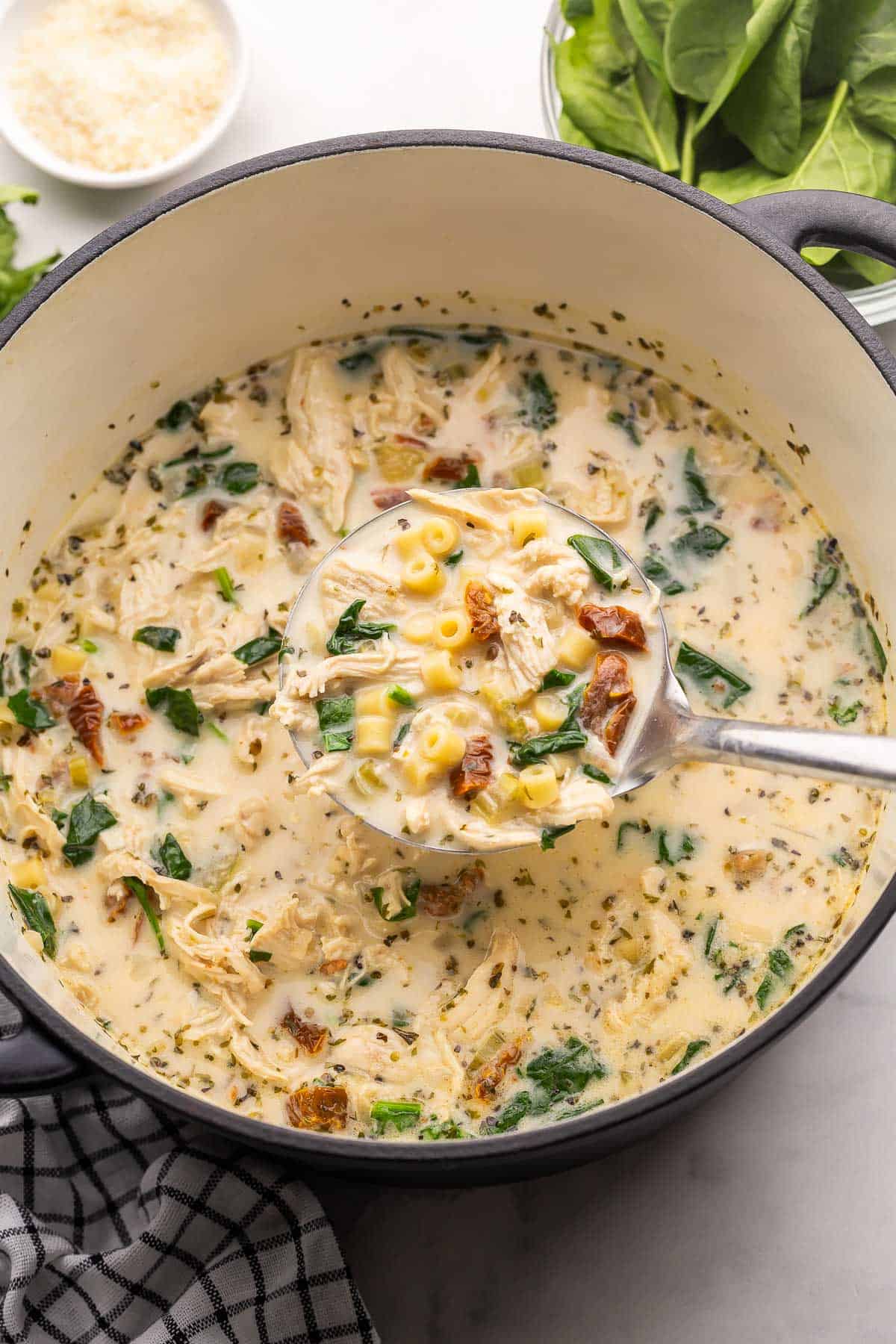 tuscan chicken noodle soup in a large dutch oven with ladle.