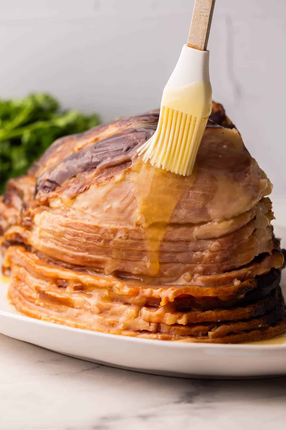 This Crockpot Ham with Pineapple Brown Sugar Glaze is tender, juicy, and incredibly simple. You only need 5 minutes of prep, while the slow cooker takes care of the rest for a flavorful main dish that fits holidays or weeknights! #slowcooker #crockpot #dinner #recipe | easy dinner recipes | dinner ideas | ham recipe | christmas dinner | easter dinner | ham recipe | spiral ham ham on a white platter with glaze being spread on.