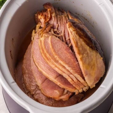 full cooked ham in white crockpot.