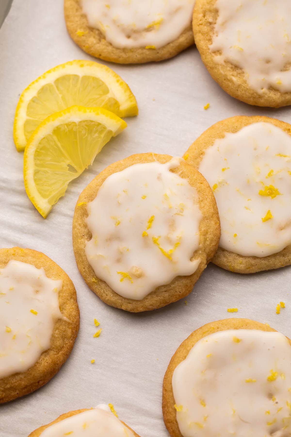 close up image of glazed lemon cookies on sheet pan with lemon slices.
