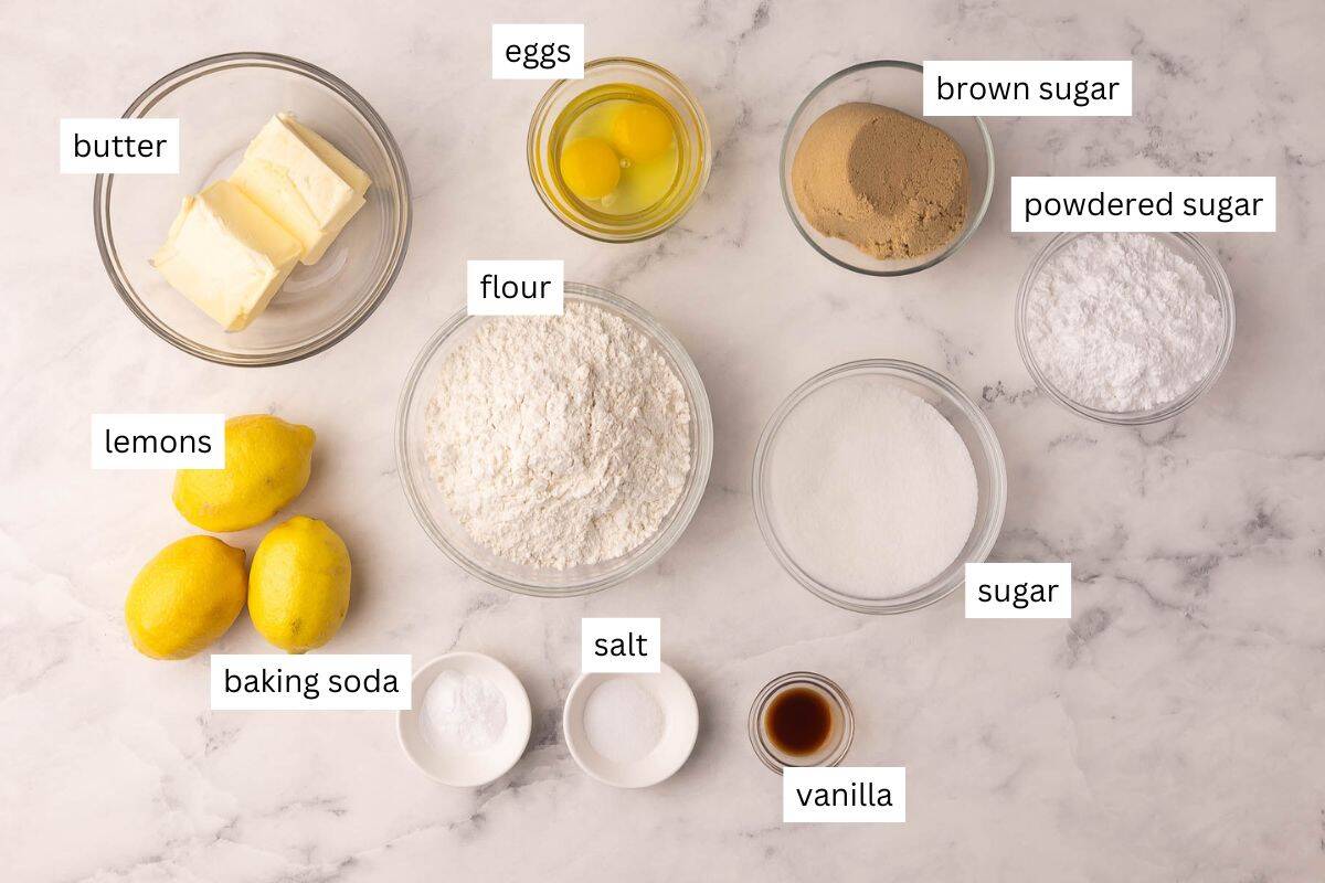 ingredients for glazed lemon cookies on a white marble background.