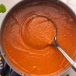 a steel ladle in a large pot of tomato soup.
