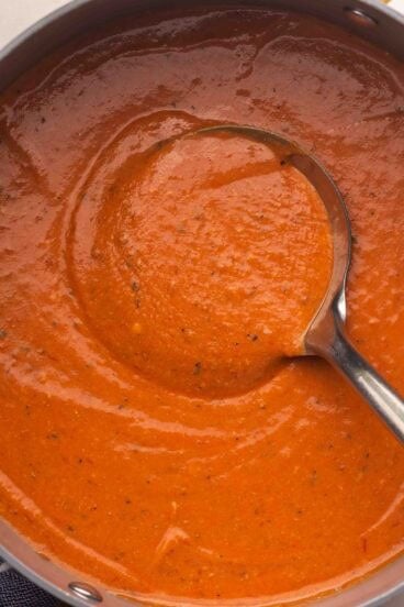 a steel ladle in a large pot of tomato soup.
