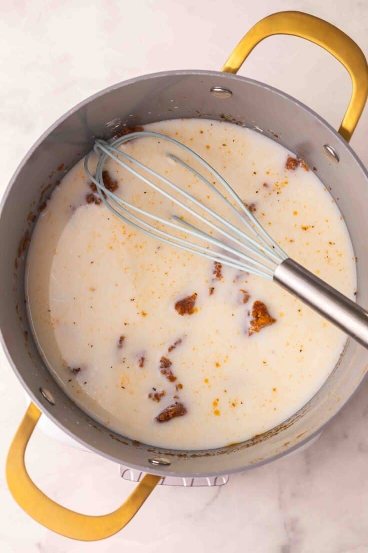 milk added to soup pot with whisk in it.
