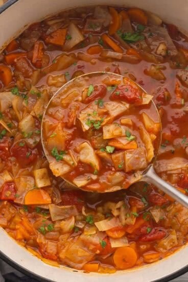 square image of metal ladle scooping cabbage soup from dutch oven.